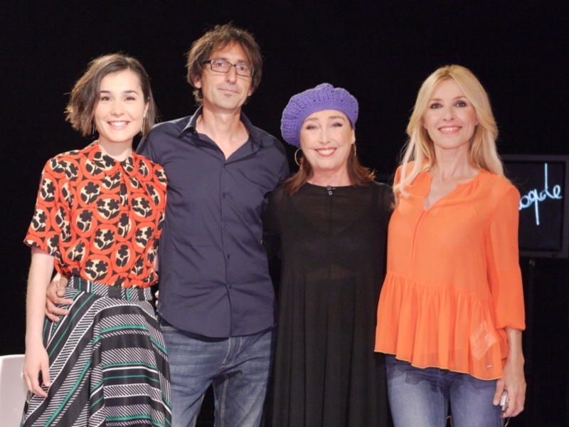 Tres personas posando juntas en un evento, con una mujer en el centro con una bufanda azul y dos mujeres a sus lados con vestidos de colores vibrantes.