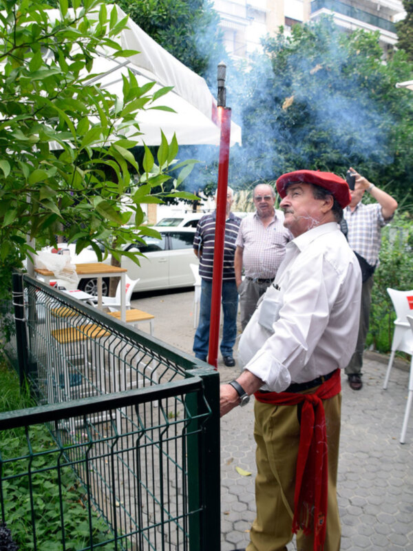 Hombre con sombrero rojo y camisa blanca observando humo en un evento al aire libre.