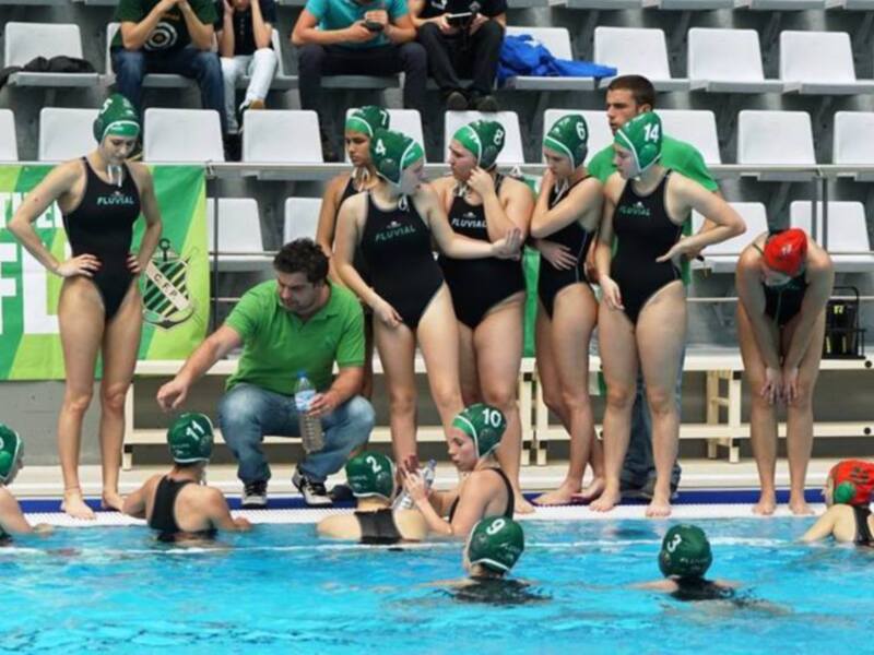 Equipo de waterpolo en el banquillo, preparándose para el juego en una piscina cubierta.