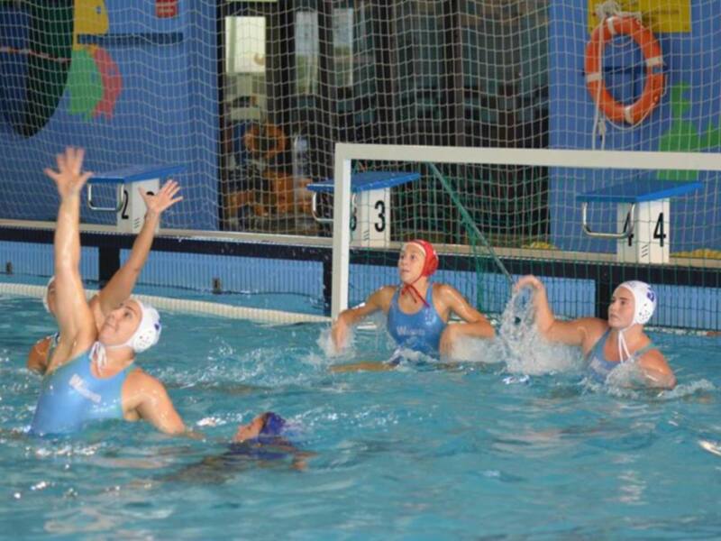 Jugadoras de waterpolo en acción durante un partido en una piscina cubierta.