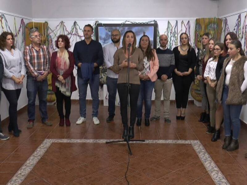 Persona hablando en un evento público con un grupo de personas alrededor, en un espacio decorado con cintas y telas.