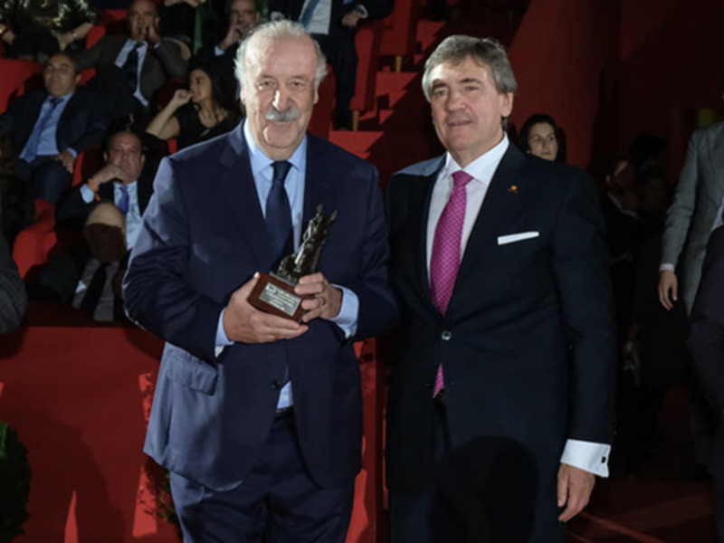 Dos hombres en trajes celebran un premio en una ceremonia formal.