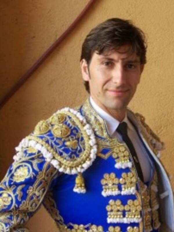 Elegante figura de un torero en traje tradicional, posando con orgullo frente a una pared amarilla.