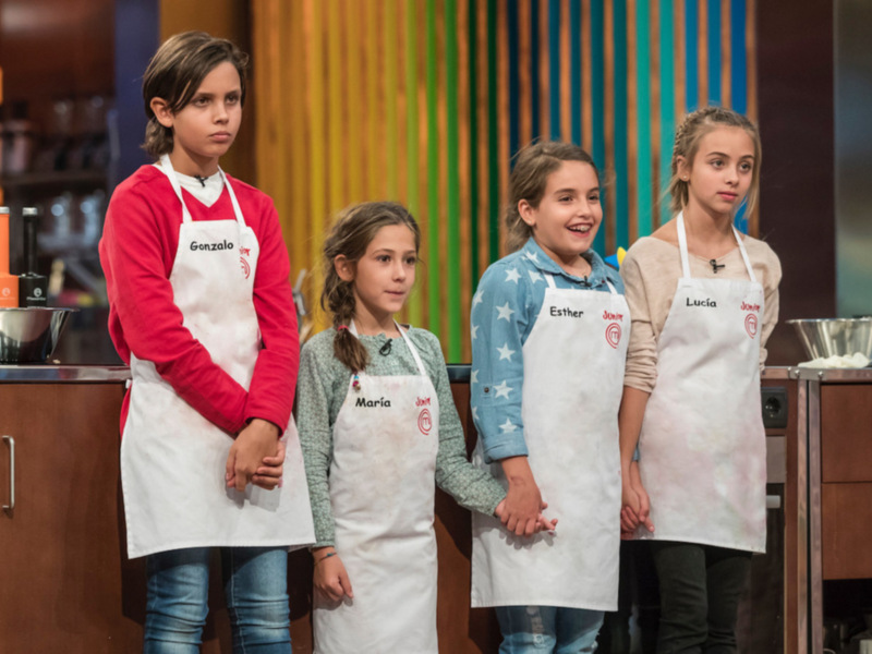 Cuatro niños participantes en un concurso de cocina, listos para comenzar.