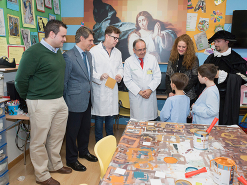Un grupo de personas, incluyendo médicos y niños, interactúan en un espacio creativo con pinturas y materiales artísticos.