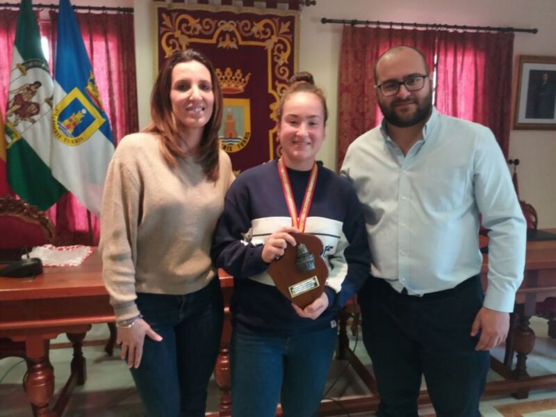 Tres personas posan para una foto en un entorno formal, una de ellas sostiene un trofeo.