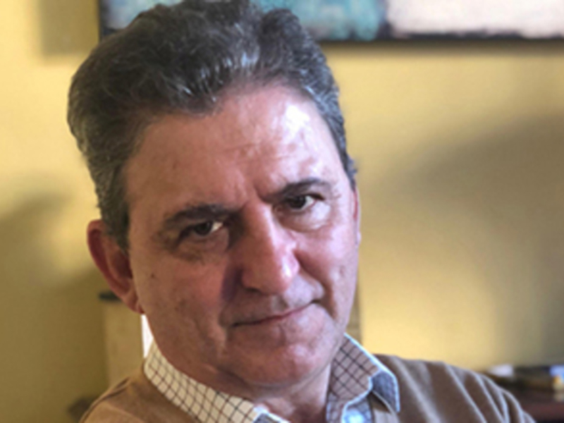 Retrato de hombre con cabello oscuro y camisa a cuadros, fondo amarillo suave.