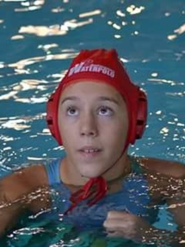 Un niño en una piscina con un casco de natación rojo y una camiseta azul.