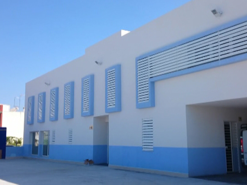 Fachada de un edificio blanco con detalles azules, ventanas y puertas abiertas.