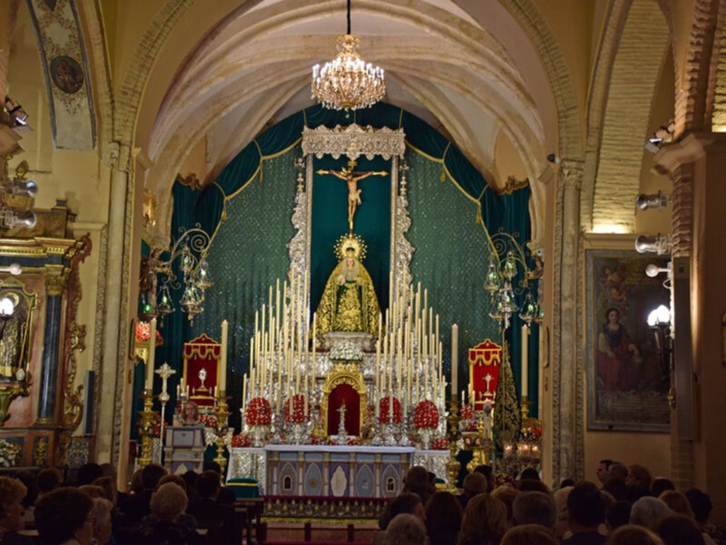 Interior de una iglesia con altares y velas, iluminado por una gran lámpara de cristal colgante.