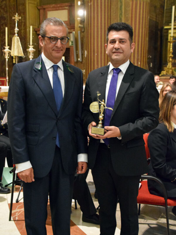 Dos hombres en trajes formales posan para una foto en una ceremonia de premiación en un ambiente formal.