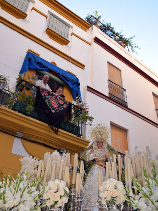 Procesión de la Virgen con flores y velas en un entorno urbano.