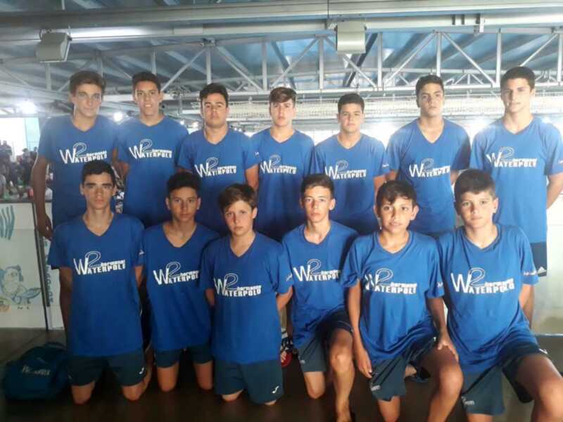 Equipo de waterpolo juvenil en uniforme azul, posando juntos en una piscina cubierta.