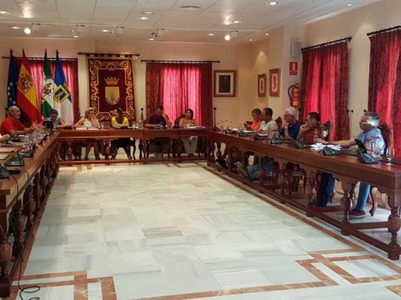 Sala de reuniones con mesa central, sillas alrededor y cortinas rojas. Bandera española y banderas de Portugal en la pared. Personas sentadas, probablemente en una sesión de trabajo o reunión oficial.