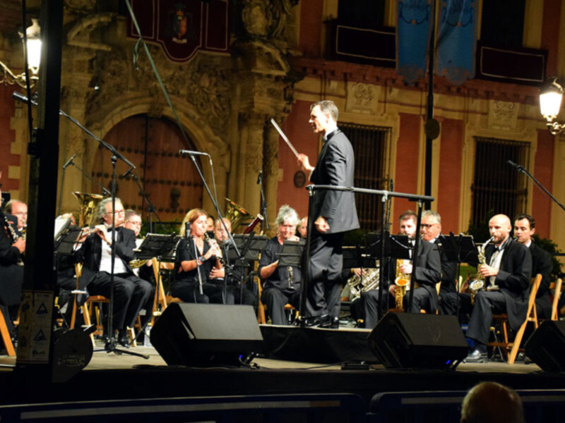 Orquesta en concierto en un escenario histórico con músicos tomando notas y un director de orquesta al frente.