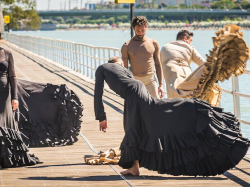 Baile flamenco en un muelle junto al río, con vestidos negros y detalles dorados.