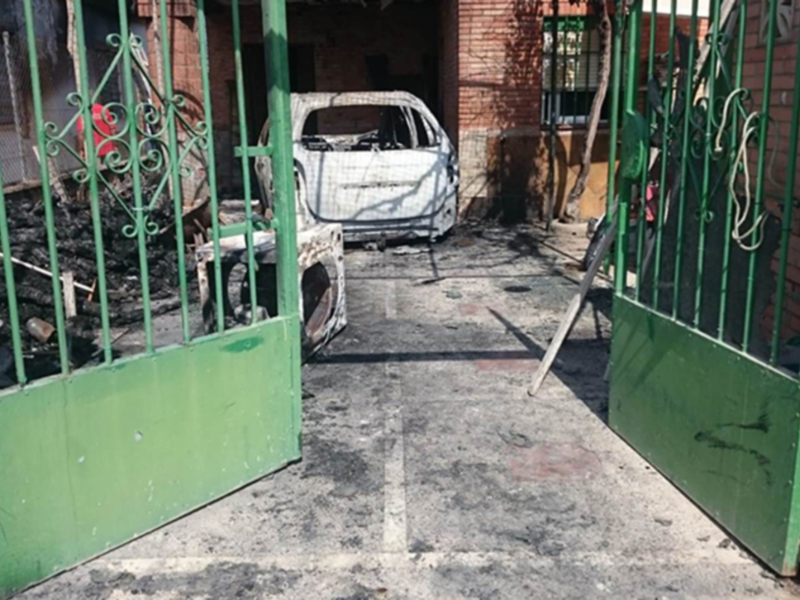 Puerta verde abierta con una bicicleta y un coche blanco en el interior, junto a una pared de ladrillo rojo.