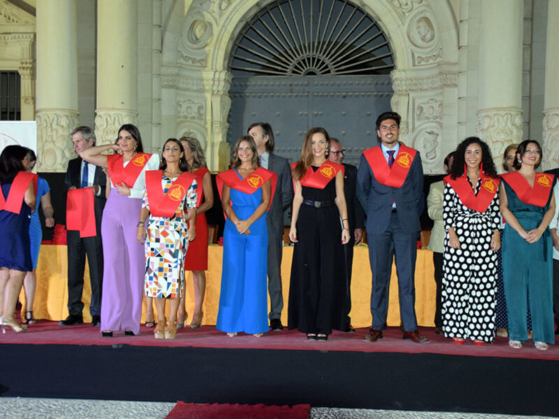 Gratuitas celebrando un evento formal en un escenario con arco y columnas antiguas.
