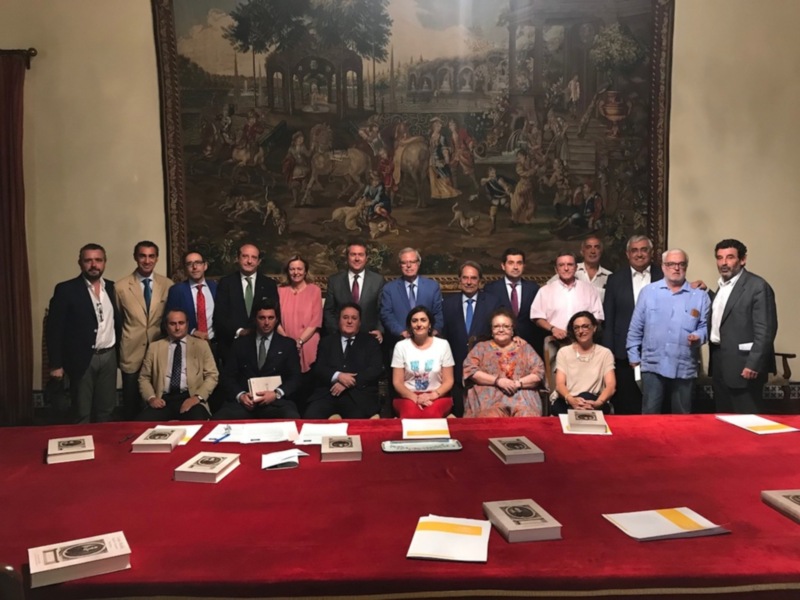 Reunión de profesionales en un salón con pintura histórica de fondo.