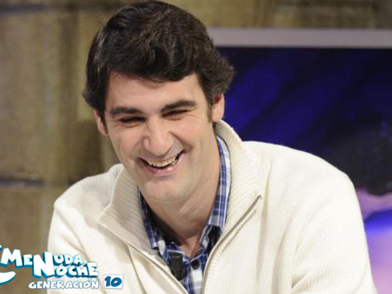 Persona sonriente en un programa de televisión, con fondo de estudio y logo de 'Menú de la Noche' visible.