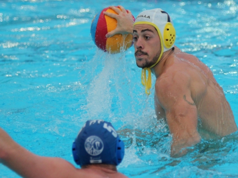 Jugador de waterpolo en acción, preparándose para golpear la pelota con la palmera en una piscina azul brillante.