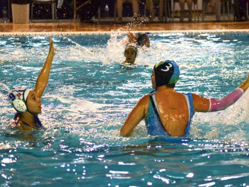 Jugadores de waterpolo en acción durante un partido nocturno en una piscina.