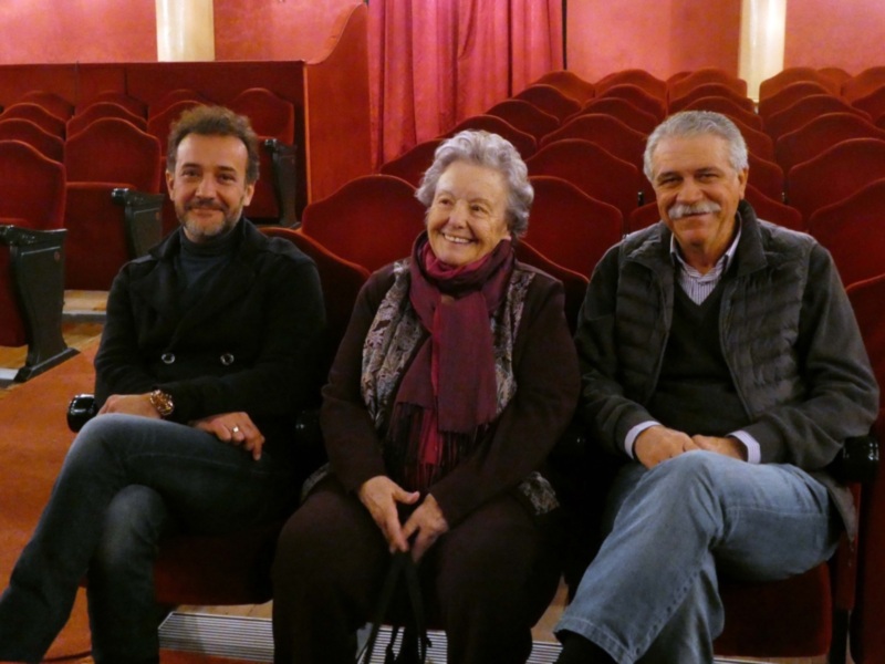 Tres personas sentadas en un teatro con butacas rojas, sonriendo y disfrutando del ambiente.