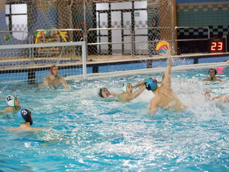 Jugadores de waterpolo compiten intensamente por el balón en el centro de la piscina.
