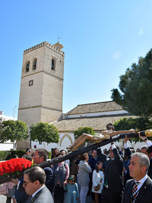 Procesión religiosa con una imagen de Cristo en la cruz, frente a una iglesia histórica con torre de ladrillo.