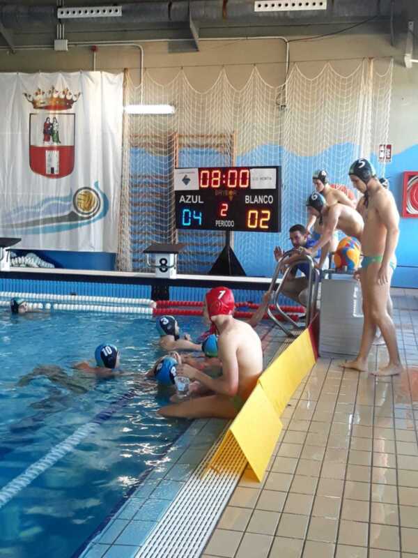 Equipo de waterpolo azul y blanco en una piscina, con marcador mostrando el resultado del partido.