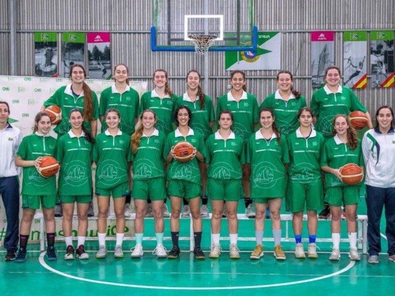 Equipo de baloncesto femenino en uniforme verde posando en cancha de baloncesto.