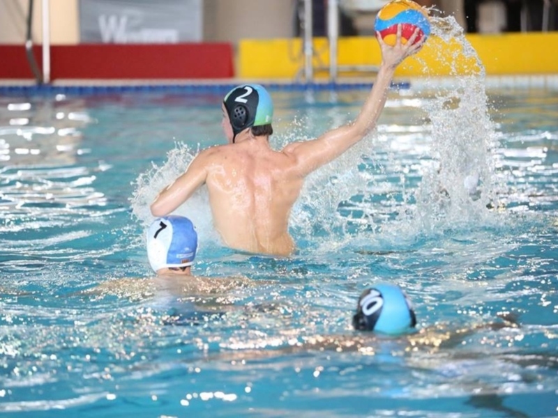 Jugador lanzando el balón en un partido de waterpolo en piscina.