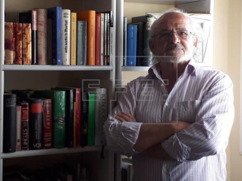 Hombre con brazos cruzados frente a una estantería llena de libros.