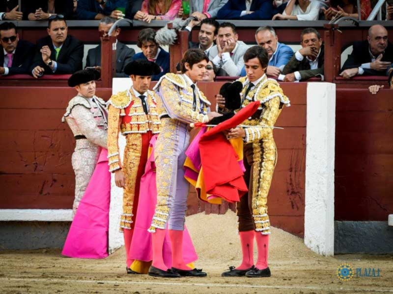 Tres matadores en trajes de lujo esperando en el ruedo de la plaza de toros.