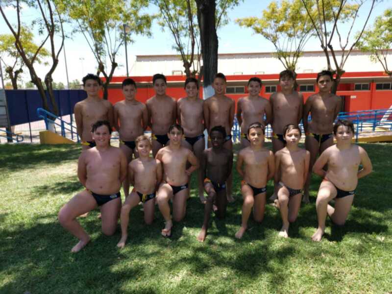 Equipo de natación infantil posando juntos en un día soleado al aire libre.
