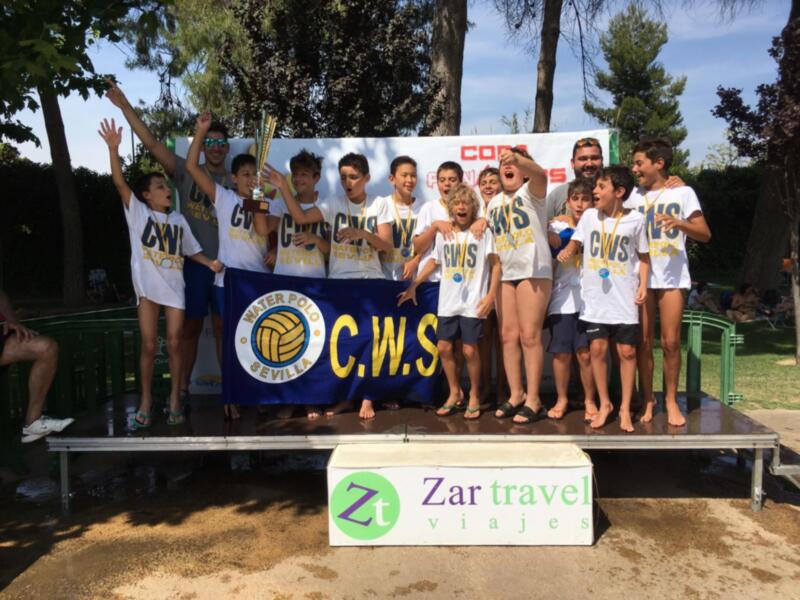 Equipo de natación celebrando su victoria en un torneo de waterpolo, con una bandera del club de natación de Sevilla en el fondo.