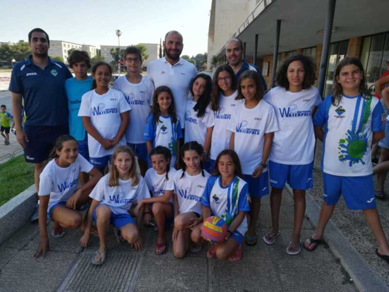 Equipo de waterpolo infantil posando juntos con su entrenador en una actividad al aire libre.