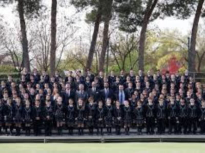 Grado de estudiantes en uniforme escolar en una cancha deportiva al aire libre.