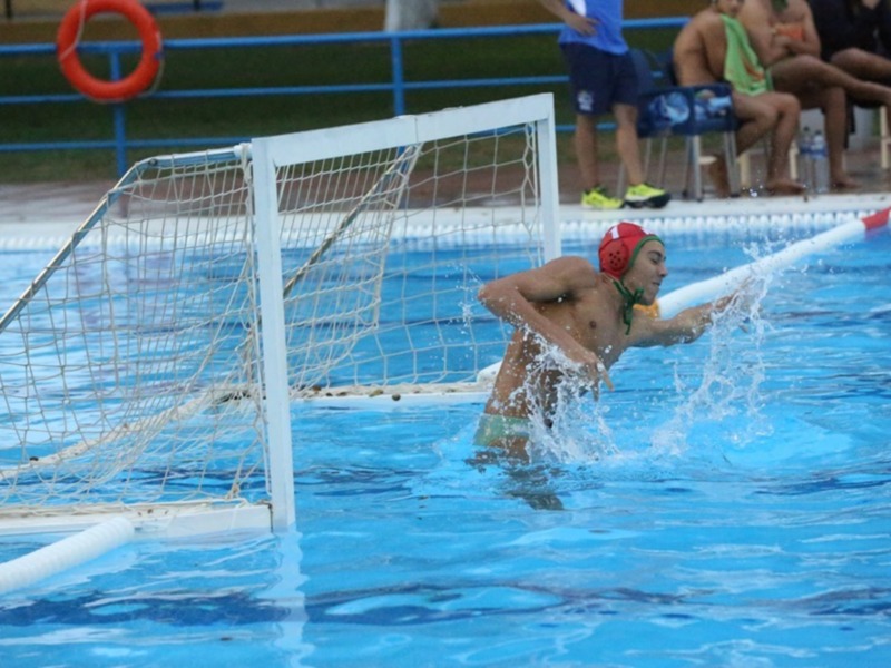 Jugador de waterpolo en acción, golpeando el balón cerca del arco en una piscina.