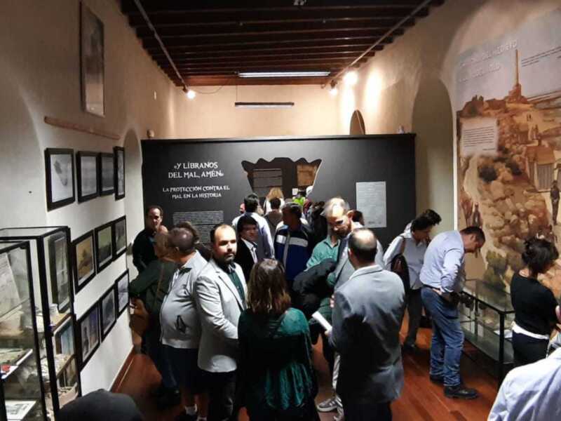 Exposición histórica en un museo, con visitantes observando información sobre la protección contra el mal en la historia.