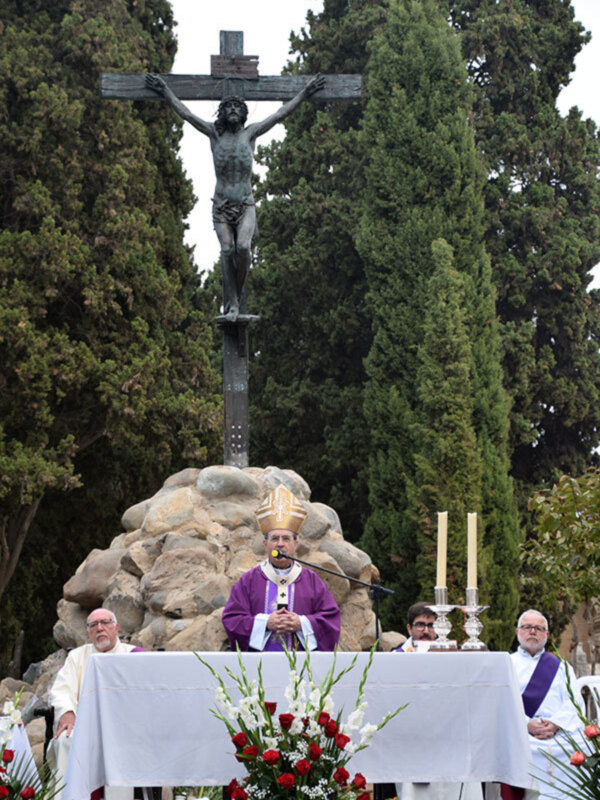 Una celebración religiosa en un cementerio, con un altar adornado y una estatua de Cristo crucificado en el centro.