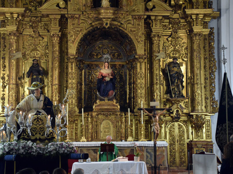 Altar dorado con estatuas religiosas y flores en el altar.