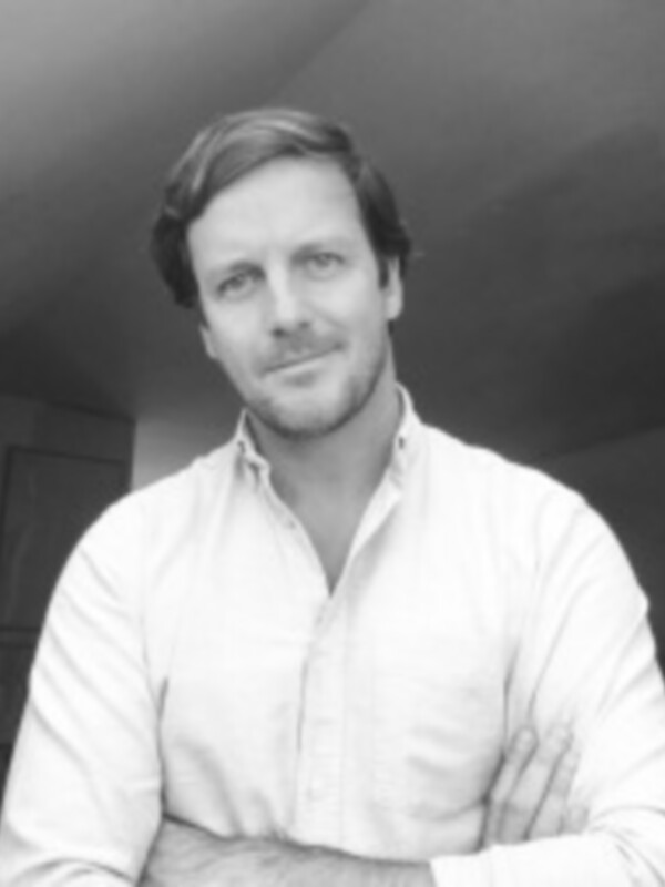 Retrato en blanco y negro de una persona con camisa blanca, posando con los brazos cruzados.