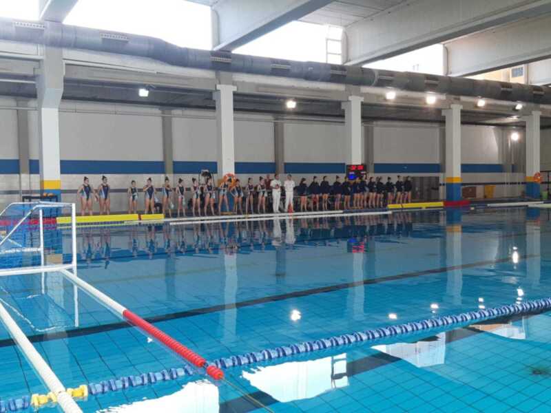 Equipo de natación en fila en una piscina cubierta, listo para una competición o práctica.