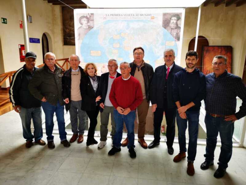 Grupo de personas posando frente a un mapa de la primera vuelta al mundo.