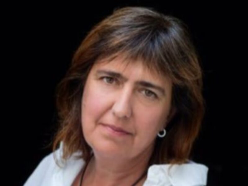 Retrato de mujer con cabello largo y lacio, vistiendo una blusa blanca y pendientes, contra un fondo oscuro.