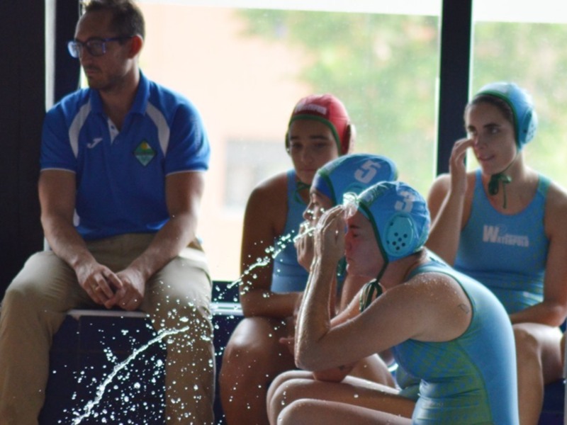 Entrenamiento de waterpolo: equipo femenino y entrenador en el borde de la piscina.