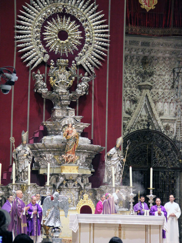 Imagen de un altar en una iglesia con estatuas religiosas y una bandera roja.