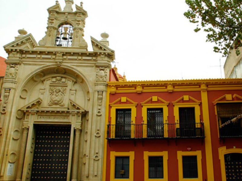 Fachada histórica con arco de entrada y detalles ornamentales en un edificio de color rojo y amarillo.