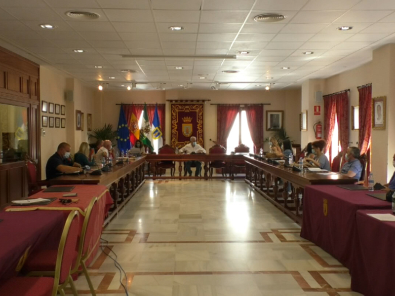 Sala de reuniones con mesas largas y sillas, decoración con banderas y cortinas rojas, y personas sentadas en las mesas.